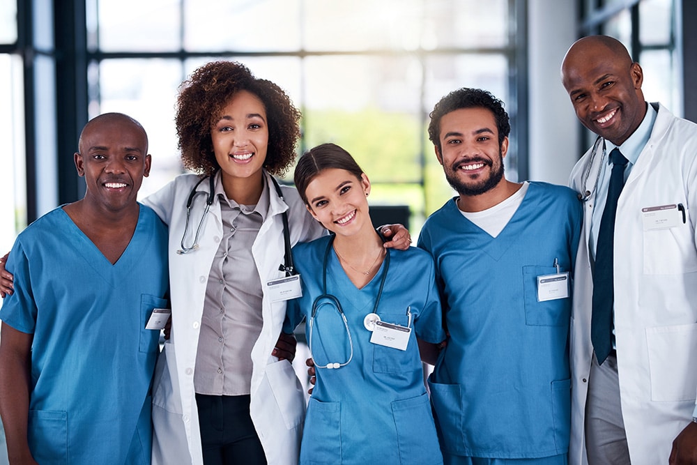 Portrait of a cheerful group of doctors standing with their arms around each other inside of a hospital during the day.